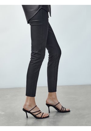 Czarne, dopasowane spodnie wykonane z gładkiego, elastycznego materiału, zestawione z czarnymi sandałami na obcasie z paskami. Strój charakteryzuje się elegancką sylwetką.