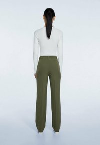 Un haut blanc côtelé à manches longues associé à un pantalon large taille haute en vert olive, avec un tissu lisse et des lignes épurées.