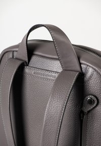 Zaino in pelle grigia con finitura testurizzata, manici superiori e dettagli di cucitura a contrasto, dotato di chiusura con zip e accentuazione del marchio.