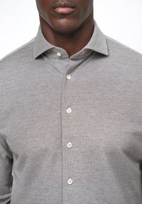 Camicia button-up grigio chiaro con tessuto texturizzato, colletto strutturato e bottoni bianchi, caratterizzata da un motivo sottile su tutta la superficie.