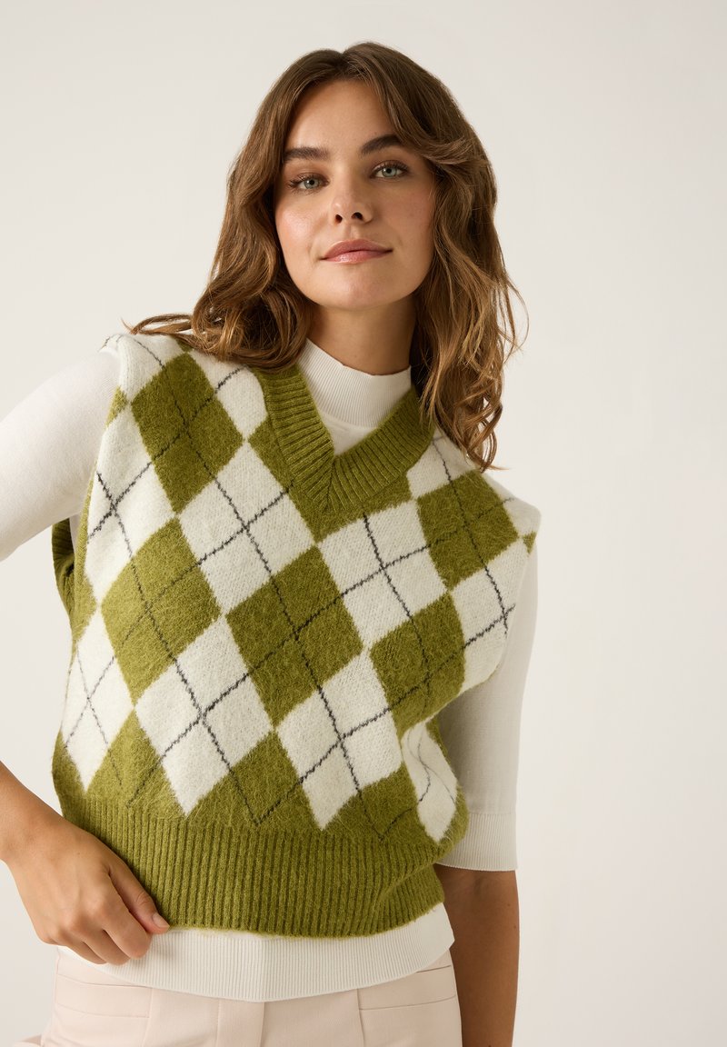 Grünes und weißes Argyle-Strick-Weste mit V-Ausschnitt und geripptem Saum. Darunter ein schlichtes weißes Langarmshirt. Weiche Textur, lässiges Design.