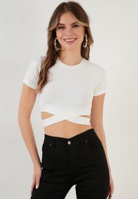 Valge soonikuga lühikese varrukaga crop top, millel on ristdisain vöökohal. Kombineeritud kõrge talje mustade teksadega.