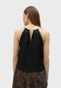 Black silk tank top with gathered neckline and keyhole back detail. Accompanied by animal print pleated skirt. Gold accents on straps.