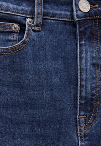 Détail d'un jean en denim bleu foncé montrant la poche avant, la petite poche à monnaie, la boucle de ceinture, les coutures orange, ainsi que le bouton et les rivets en métal.