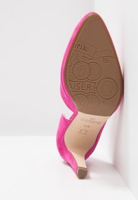 Chaussure à talon aigu en daim rose avec un bout pointu et un design découpé. La semelle présente des éléments décoratifs en relief et le nom de la marque.