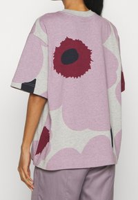 Oversized t-shirt w kolorze jasnoszarym i mauve, z dużymi bordowymi wzorami kwiatowymi. Wykonana z miękkiej bawełny, z okrągłym dekoltem i krótkimi rękawami.