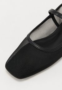 Ballerines noires avec un bout carré, dessus en tissu comportant un détail en maille, et une bande fine sur le coup de pied. Texture lisse sur l'ensemble.