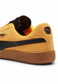 PUMA gele suede sneakers met een zwarte streep, voorzien van een rubberen zool en zwarte accenten op de hak en de tong.