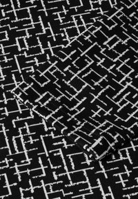 Schwarzer Stoff mit einem weißen abstrakten geometrischen Muster, das eine weiche Textur und einen gefalteten Rand aufweist, der filigrane Liniendetails betont.