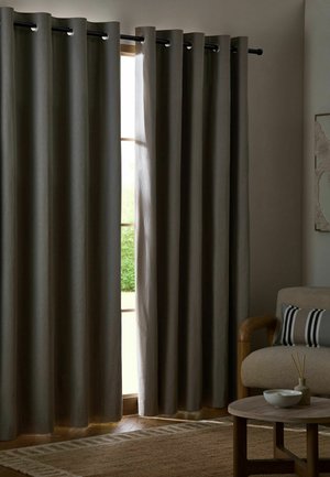 Gray curtains partially open on a window in a living room with a beige armchair, striped pillow, wooden coffee table, and neutral rug.