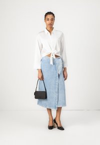Camicia bianca con bottoni annodata in vita, gonna avvolgente in denim azzurro chiaro, scarpe col tacco nere e una piccola borsa nera.