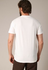T-shirt blanc à manches courtes en coton doux, avec un col rond et un design uni, sans motifs ni graphiques visibles.