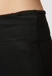 Lähikuva mustista korkeavyötäröisistä legginsseistä, jotka näyttävät kankaan tekstuurin, ompeluyksityiskohtia ja osan paljaasta vyötäröstä.