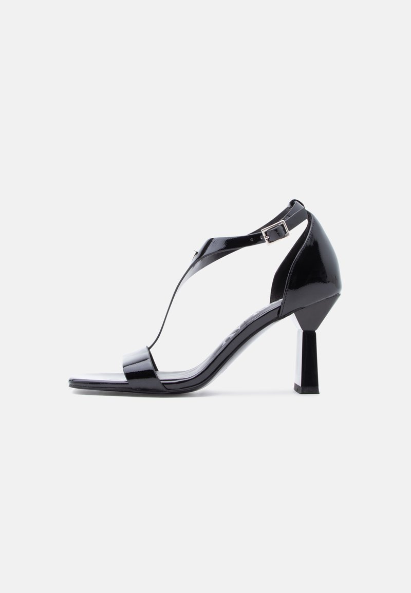 Μαύρα γυναικεία σανδάλια με ψηλό τακούνι από πατενταρισμένο δέρμα, με σχεδιασμό T-strap, τετράγωνη μύτη και χοντρό τακούνι για σταθερότητα. Ρυθμιζόμενο κούμπωμα στον αστράγαλο.