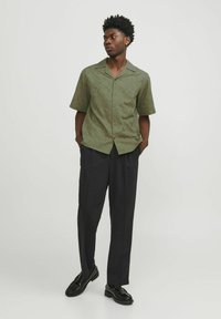 Korte mouwen knop-sluiting shirt in olijf groen met een geometrisch patroon; gecombineerd met zwarte broek en zwarte schoenen.