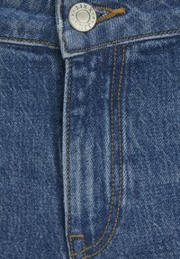 Džinsinis audinys su mėlynu atspalviu, turintis metalinį mygtuką ir kontrastingus geltonus siūlus aplink liemenį ir šoninius siūlus.