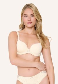 Jasnożółty wyściełany biustonosz z koronkowymi akcentami i ozdobną kokardką na środku; posiada regulowane ramiączka oraz gładką, teksturowaną tkaninę.