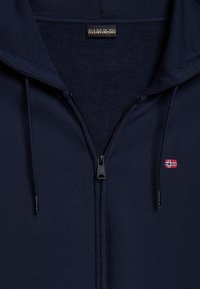 Felpa con zip di colore blu navy, con interno texturizzato, caratterizzata da una chiusura con zip, una bandiera norvegese ricamata e un'etichetta con logo sul colletto.