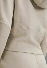 Tissu de sweat beige montrant des coutures détaillées et une texture côtelée sur le bas du dos et les manches.