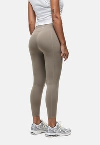 Beige leggings met een gladde, aansluitende pasvorm en subtiele stikdetails, gecombineerd met grijze en witte hardloopschoenen.