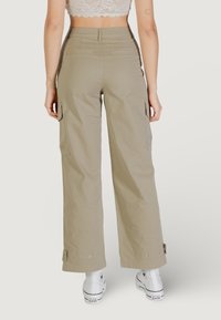 Pantalones cargo beige con piernas anchas, que cuentan con bolsillos laterales, puños ajustables y una textura suave. Combinados con zapatillas blancas.