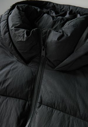 Giacca a vento nera con colletto alto, zip a tutta lunghezza e texture leggera e stropicciata. Gli accenti includono una zip lucida e cuciture.