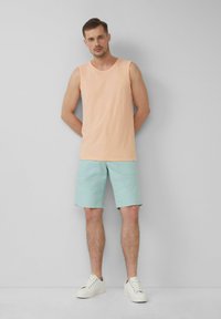 Débardeur pêche, shorts bleu clair avec une texture subtile, associés à des baskets blanches. Design simple, sans motifs ni accents visibles.
