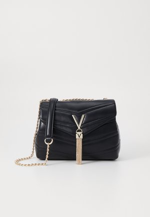 Bolsa de mão de couro preto com design acolchoado, alça de corrente dourada e detalhe em metal em forma de V com tassel. Forma retangular compacta.