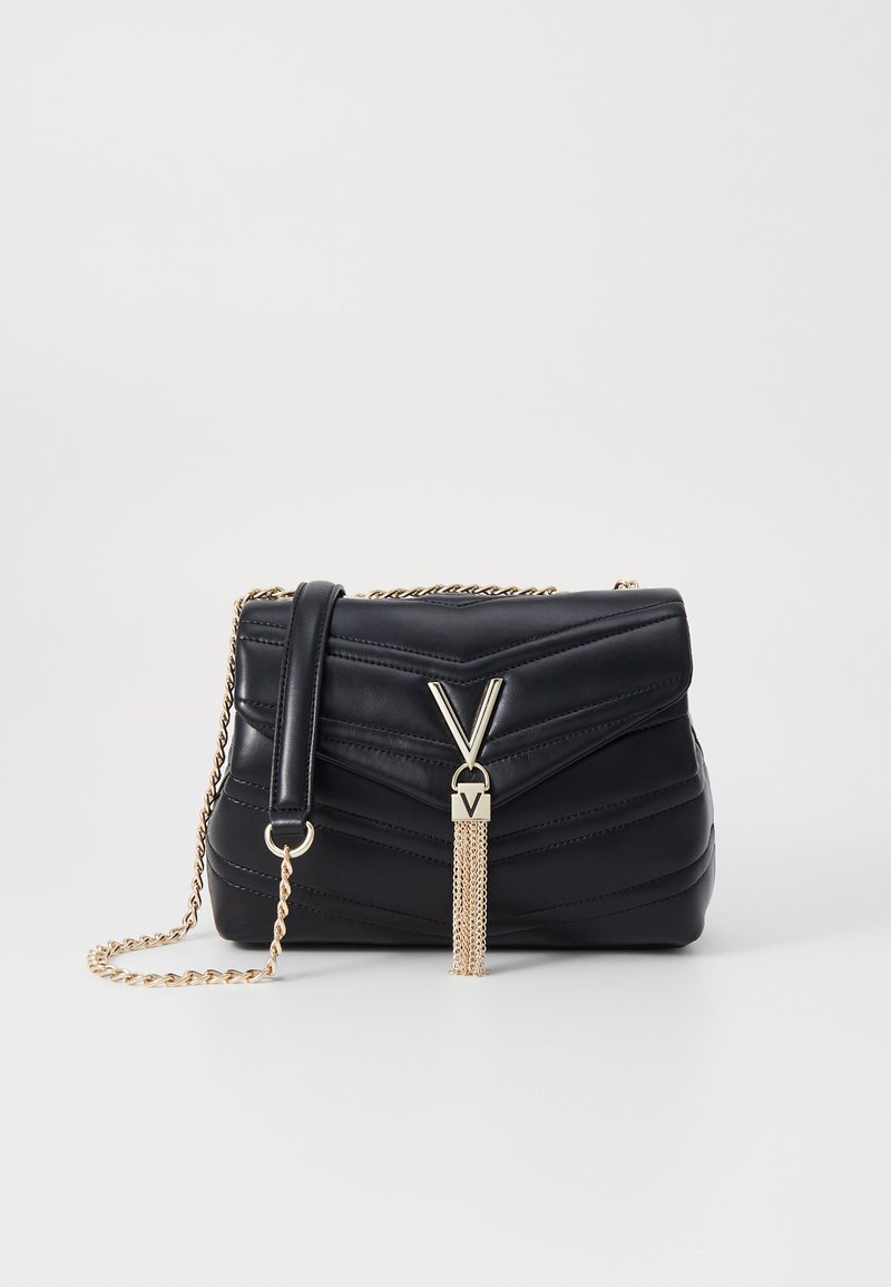Black leather handbag with quilted design, gold chain strap, and metal V-shaped accent with tassel detail. Compact rectangular shape.