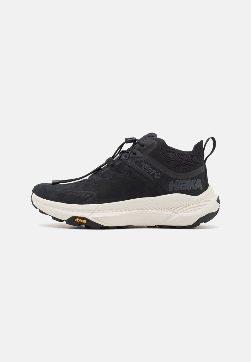 Pantofi sport negri cu un br Faten texturat, talpă intermediară albă și talpă Vibram. Au un sistem de șireturi și un cablu de tragere la călcâi.