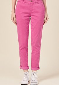 Bright pink cotton chinos with a slim fit, featuring a button closure and rolled cuffs. Paired with white high-top sneakers.