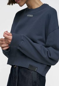 Felpa a maniche lunghe blu navy con polsini e colletto a costine. Presenta la scritta ricamata "10DAYS" sul davanti e un'etichetta sull'orlo. Texture morbida.