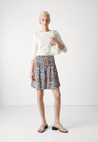 Top blanco de manga larga combinado con una falda de patrón floral multicolor con cintura fruncida. Llevado con sandalias beige de tiras.