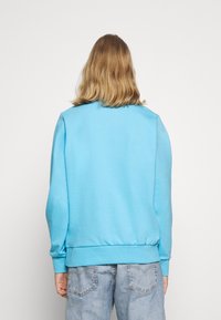 Světle modrá mikina s žebrovanými manžetami a lemem, vyrobená z hladkého bavlněného materiálu, s volným střihem a bez viditelných vzorů nebo grafik.