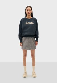 Felpa blu scuro con la scritta "Love" in crema, abbinata a una gonna di jeans grigia. Calzini alla caviglia crema e sneakers beige completano l'outfit.