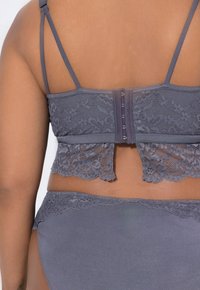 Bralette in pizzo grigio con spalline regolabili, dotato di chiusura a gancio e occhiello e orlo in pizzo scallopato. Slip coordinato con rifiniture in pizzo.
