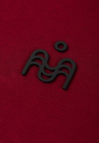 Bordeauxrode stof met een gestructureerde afwerking, met een verhoogd zwart logodesign dat gestileerde letters en een cirkelvormig accent bevat.