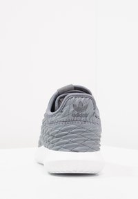 Grå vadderad sneaker med quiltad textur, som har en rundad klack, vit gummisula och tonal logobroderi på baksidan.