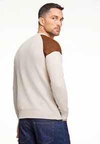 Pullover mit gerippter Struktur in hellbeige, mit braunem Wildleder an den Schultern. Mit einem Rundhalsausschnitt und einem eng anliegenden Saum gestaltet.