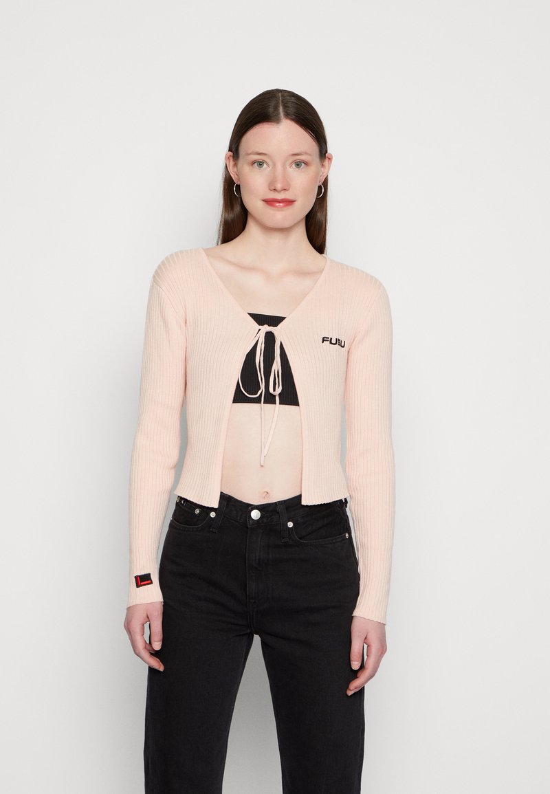 Hele roosa ribaga kardigan V-kaelusega, esipoolse lipsuga detailiga ja tikandiga logoga. Kombineeritud mustade kõrge vöökoha teksadega.