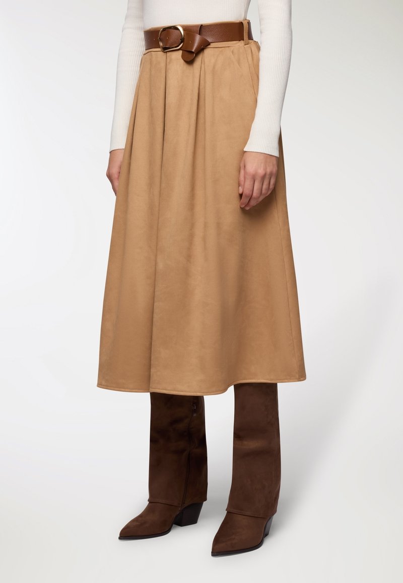 Gonna midi in suede color marrone chiaro con un design fluido e una cintura in pelle marrone con fibbia dorata. Abbinata a stivali a ginocchio con tacco marroni.
