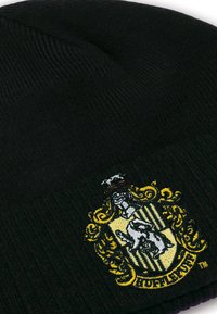 Schwarze Strickmütze mit einem bunten gestickten Hogwarts-Wappen, das einen Dachs zeigt, umgeben von kunstvollen goldenen Akzenten und schwarzen Streifen.