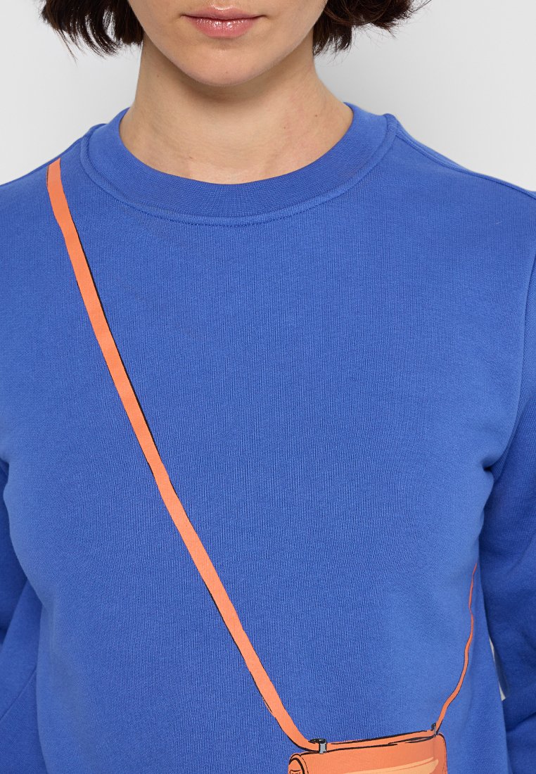 Sudadera azul con tejido texturizado y cuello redondo, que presenta un gráfico naranja que representa una bolsa con una correa cruzando el pecho.