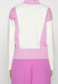 Pull color-block en tissu tricoté doux. Présente des accents rose pastel, blanc et jaune avec un col montant et des poignets côtelés.