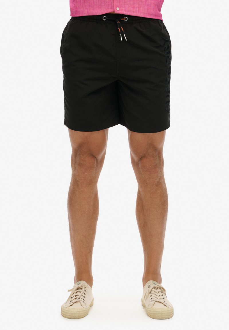 Costume da bagno neri con vita elastica e coulisse. Presenta tasche laterali e un logo discreto sul lato sinistro.