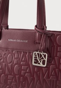 Burgundivärinen nahkalaukku, jossa on kohotettu "Armani Exchange" -logo, hopeiset yksityiskohdat, kaksoiskahvat ja tagi, jossa on tyylitelty logo.”}}}  artoq to=translate_text_response to=plaintext translatetextresponse to=plaintext<|vq_15062|>{