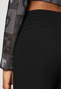 Zwarte legging met textuurdetail op de tailleband en een geperforeerde stofafwerking aan de bovenkant, die verschillende zwarte tinten toont.