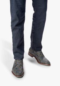 Chaussures à lacets texturées avec un motif multicolore, dotées d'un petit talon et d'un bout arrondi. Portées avec un pantalon marine foncé.