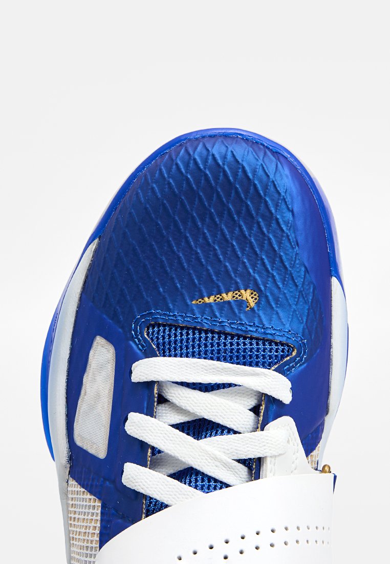 Niebieski but sportowy z teksturowaną cholewką, białymi sznurówkami, siateczkowymi akcentami i złotym detalem logo. Podeszwa jest biała z zaokrąglonym kształtem.