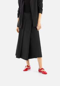 Jupe midi plissée noire avec une large taille, accompagnée de chaussures Mary Jane rouges brillantes avec une lanière et un bout rond.